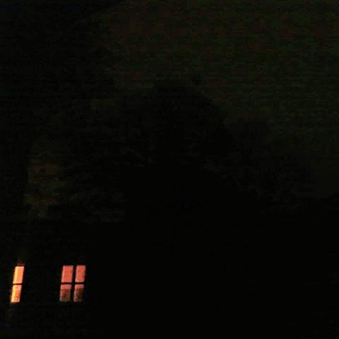 a dark house under a dark sky, two windows are illuminated with red light