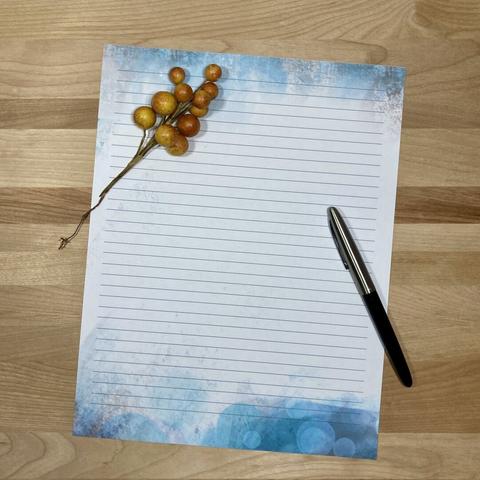 Photograph of a piece of stationery paper on a wooden surface, posed with a pen and a sprig of berries.