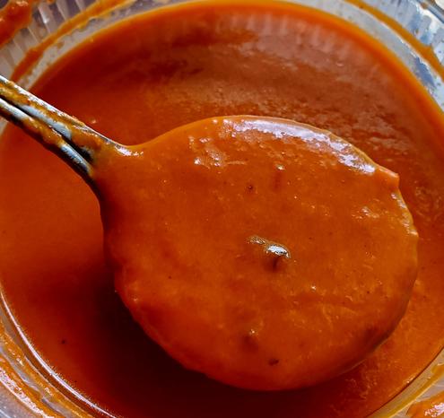 Indian style, tomato soup - pureed texture. In plastic container. Soup spoon with soup is raised