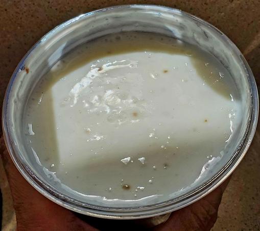 Salt lassi - in plastic cup. White yogurt based drink, with cumin, black salt & mint pureed together.