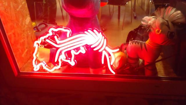 Das Logo des CCC-CH aus rot leuchtenden Streifen in einem Fenster stehend. Daneben ein rot angeleuchtetes Pony-Plüschie.