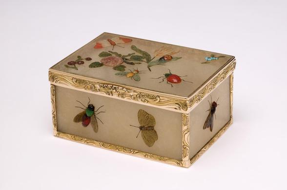 "MATERIALS AND TECHNIQUES
Six panels of beige chalcedony overlaid with a variety of chalcedonies, agates including red-tinted banded agate, bloodstone, red jasper, turquoise and lapis lazuli, with later glass and stone replacements; chased gold mounts.
PHYSICAL DESCRIPTION
A rectangular, gold-mounted hardstone snuffbox formed of six panels of beige chalcedony. These are decorated with insects and flowers made of hardstone, with the details of the legs and antennae engraved and blackened. The gold mounts are chased with scrolls and flowers."
"This box, of panels of chalcedony (a type of quartz), is applied with flowers and insects in various coloured hardstones and some glass elements. The technique of raised stonework such as this is frequently associated with the court of Frederick the Great of Prussia (r. 1740-86) in Berlin, and it is likely that this box was made there.
Friedrich Ludwig Hoffmann (active c.1760–70) was active as a stone-cutter in Bayreuth, Germany, in 1762. He may have been one of a group of artists who moved to Berlin in 1763, following the death of the Margrave of Brandenburgh-Bayreuth in the same year."
View 1: side profile showing top and two sides of box