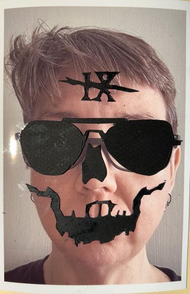 Collage in my sketchbook. A photo of a white woman with short brown hair. Over her face are pasted cut pieces of black paper: the nose and mouth of a skeleton face, aviator glasses, and a crossed out IX on her forehead.
