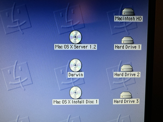 Screenshot of install CDs for three vintage OSX-related operating systems next to the hard drives they’re each about to be installed onto.