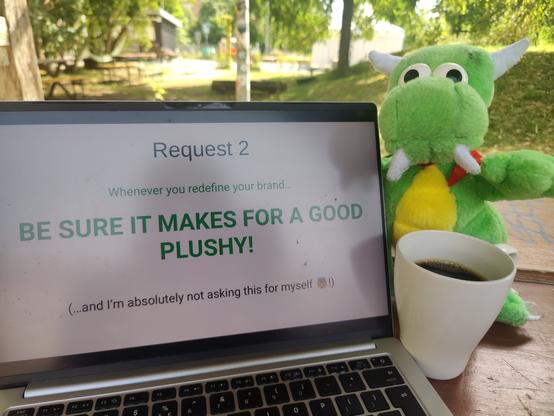 Konqi sitting next to a laptop screen with above quote, coffee cup in front and Z-Bau garden in the back