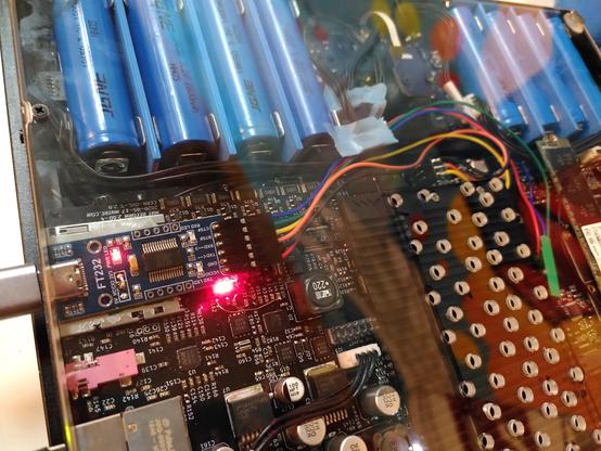 The inside of an mnt reform. A blue serial adapter has been taped to the SD card slot. A bunch of colored cables go off of it. Three of them terminate on a header.