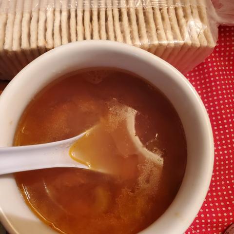 Chicken broth with tiny vegetable pieces soup. Sleeve of saltine crackers beside the bowl of soup.