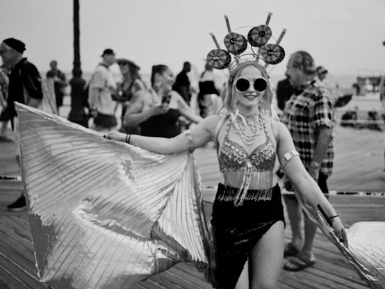 At the Mermaid Parade, a woman in festive mermaid cosplay, complete with an aquatic-themed headdress, celebrates on the boardwalk of Coney Island, Brooklyn.