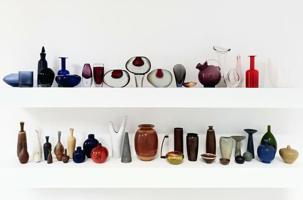 2 weiße Wandborde mit viele kunstvoll geformten Vasen, viele aus farbigem gemusterten Glas