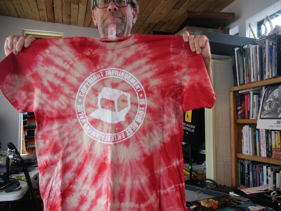 A Negativland t-shirt with their logo and the slogan "Copyright Infringement is Your Best Entertainment Value", hand tie-dyed red and off-white by Steev Hise and for sale.