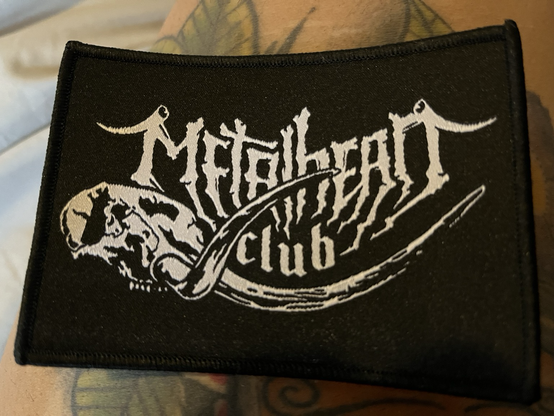 A photo of a black woven patch with white logo that says metal head club.