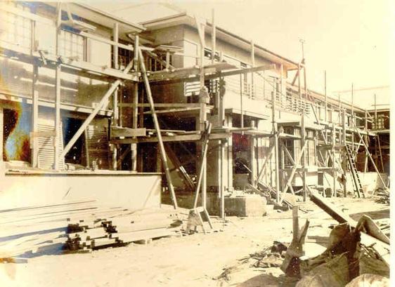 Black-and-white toned photo: Woodford House, Hawke’s Bay – Steeltex exterior, Lustre Stucco and NZ Plaster Board. 1925. Description: Shows a two-storey building under construction with wooden scaffolding along the front. Citation: The Fletcher Trust Archives, Winstone Ltd – Images of buildings using Winstone products. Registration No. P6274/80. https://collection.fletcherarchives.co.nz/objects/73946/winstone-ltd-images-of-buildings-using-winstone-products-1925-woodford-house-hawkes-bay-steeltex-exterior-lustre-stucco-and-nz-plaster-board
