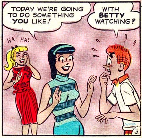 Brunette Veronica Lodge, in a turquoise sweater and skirt, is talking to her redheaded boyfriend Archie Andrews as her best frenemy, blonde Betty Cooper wearing a red dress looks on. A smiling Veronica says to Archie, “Today we’re going to do something YOU like!” A visibly terrified Archie replies, “With BETTY watching?” Betty is behind them laughing.