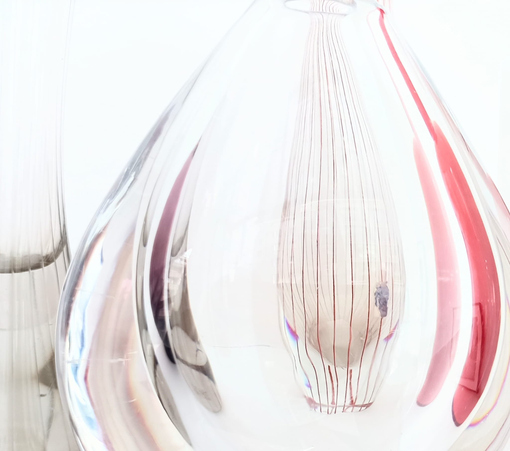 Im Vordergrund eine dicke Glasvase, dahinter, hindurch gesehen, eine andere hohe schmale Vase mit roten Streifen
