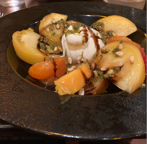 red and yellow heirloom tomatoes drizzled with balsamic vinegar dressing, dotted with pine nuts, with a big chunk of burrata cheese in the middle of the bowl.