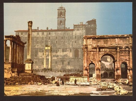 The image is of a historical architectural setting, possibly from the Roman era. It depicts ruins with various structures and arches that appear to be part of what was once significant buildings or landmarks in ancient Rome. The colors are muted, giving it an old-world look, which suggests that this may be a photograph from the late 19th century or early 20th century. There is no text present in the image. The ruins include columns and arches indicative of Roman architecture style, which were commonly used for public buildings such as temples or city gates. These structures are now partially in disrepair, indicating that they have been exposed to time and possibly some historical events leading to their current state of preservation.