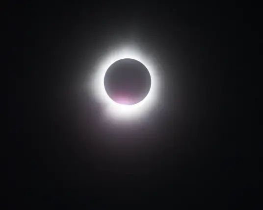 The 2024 total solar eclipse at totality with the beginnings of the full sunlight flaring pink from the bottom of the ring of light.