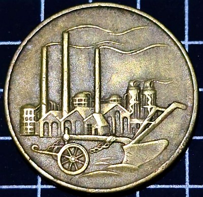 Factories with smoke coming out of chimneys, and a plow in the foreground, on a round brass-looking coin with no text on this side.  The coin is around 20 - 25mm diameter.