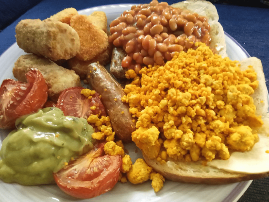 A cooked breakfast in 'traditional English' style but with a vegan twist. Grilled fresh tomatoes, potato croquettes, sweet potato hash browns, vegan sausage, baked been on toast, scrambled tofu on toast and a scoop of mashed avocado.