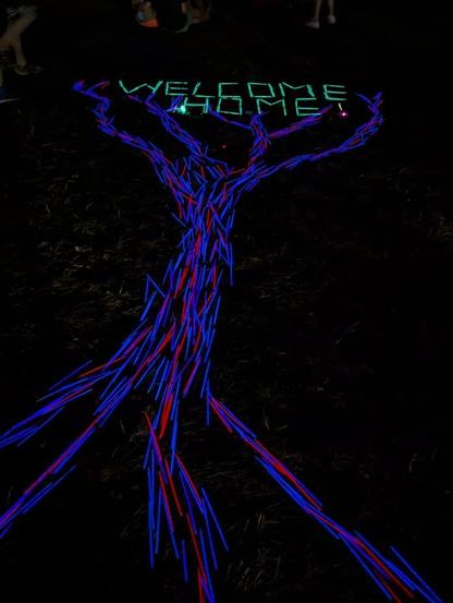 A replica tree with the words 'Welcome Home' above it made entirely from multicolored glow sticks.