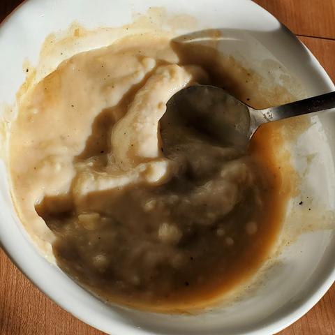 Buttered mashed potatoes with gravy in white bowl with silver plate spoon