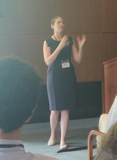 Elle O'Brien speaking at ICSSI. She's a white woman with brown hair in a bun, wearing a dark blue dress.