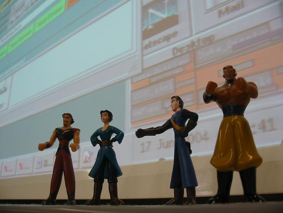 Four small Barilla Sinbad action figures standing on a small ledge in front of a computer screen. On the screen one can see a task bar, some quick launch icons, including Netscape, and the corner of  the Virgo Datadisplay tool.