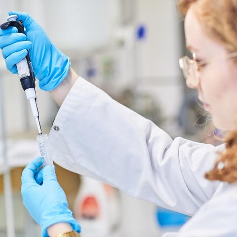 A photo of a scientist working in her lab with a syringe and test tube in her hands.