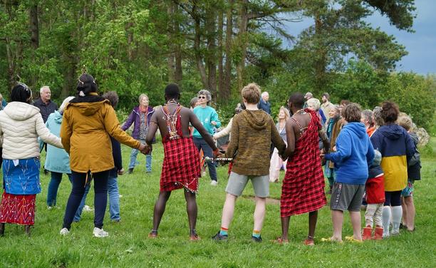 Members of Transition Chipping Norton and their Maasai visitors in traditional red checked robes hold hands in a circle as part of an event to bring them together and explore each others lives and cultures.