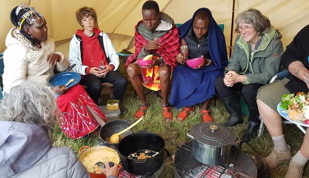 Members of Transition Chipping Norton and their Maasai visitors enjoy a hot meal served from large pans in the centre of their circle in a beige tent.