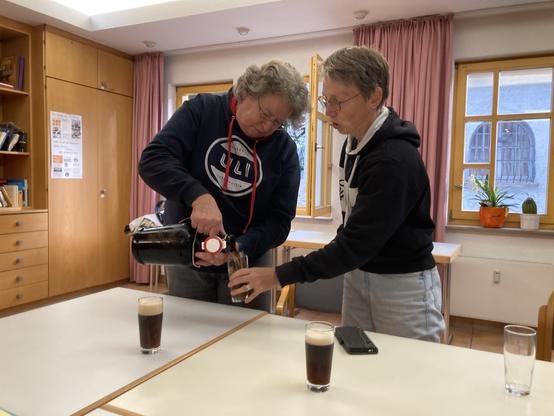 Eine Frau gießt aus einer großen Flasche Bier in ein Glas, welches von einer anderen Frau Geistern wird.