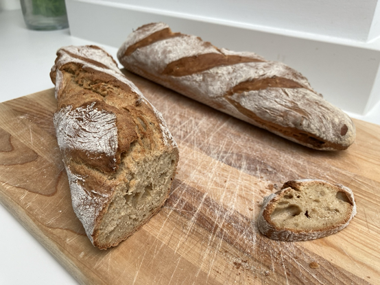 Two baguettes on a wooden board, with a golden colour and dusted with white flour.