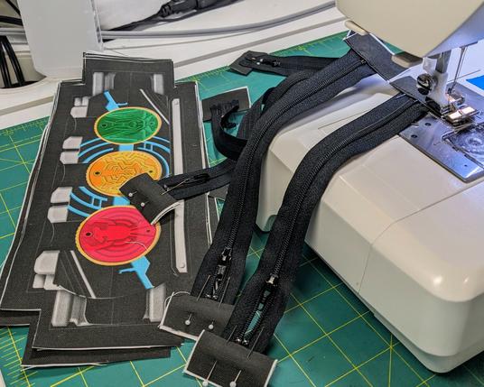 a stack of Tatoba belt pouch fronts next to a sewing machine loaded with freshly stitched zippers
