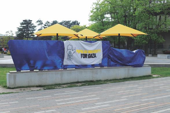 Photograph of the then-obscured 3D "Waterloo" sign on the University of Waterloo campus. The words are wrapped up with a blue tarp and a sign reading "POPULAR UNIVERSITY FOR GAZA" hangs on top.