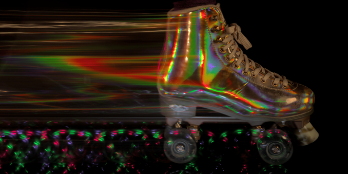 A photo of a metallic roller-skate streaking across the frame from left to right on a black background. I leaves a swooping trail of intermittent colored light dashes from the wheels, and a wing-shaped blur of varying colors from the iridescent boot material.