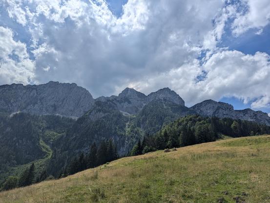 A rough limestone range framed by green grass and growing, but still pretty bright clouds