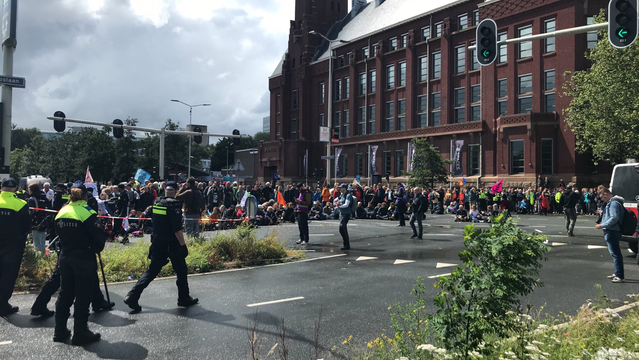 Kruispunt naar de A12 met een grote groep rebellen op het asfalt. Vooraan meerdere politieagenten.