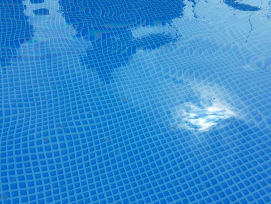 In den Pool rein fotografiert, man sieht kristall klares Wasser. Der Boden mit kleiner blauer Kacheloptik ist sehr gut und klar zu sehen.