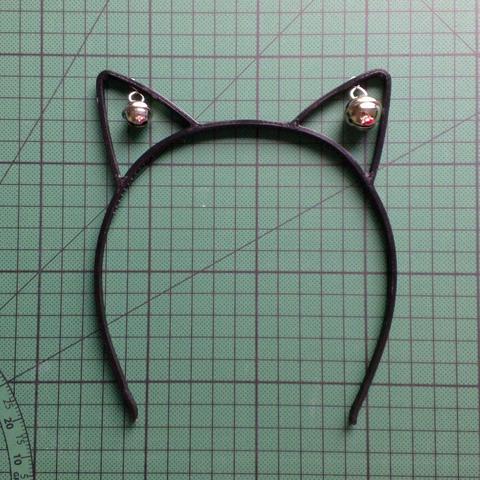 Photo of a pair of black 3D printed catears with two small metallic bells of different size, one attached to the inside of each ear.