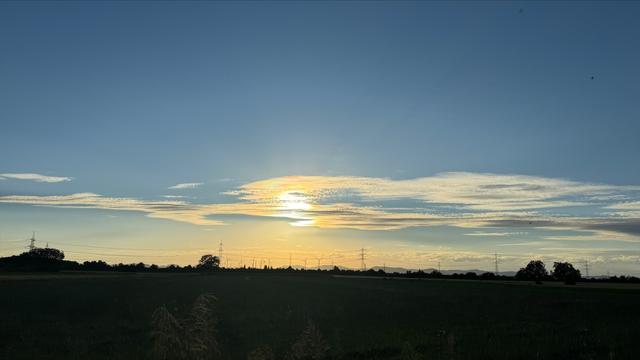 Ruhe am Abend zeigt einen Sonnenuntergang am Horizont über Windrädern und Stromleitungen