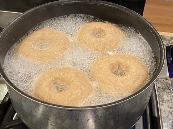four bagels boiling in a pot, the water is roiling pretty high but not out of control