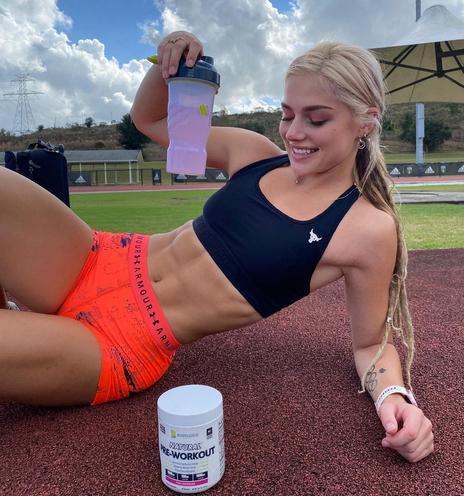 A very fit girl in sports shorts and bra lying on the tartan of a running track.