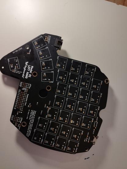 keyboard.io model 01 black pcb left half from the back. You can see the diodes and the keyswitches soldered as well as the expansion port. also a text written: "Thank you for looking inside your keyboard! Plugging stuff into the expansion port or ICSP connectors may void your warranty, but don't let that stop you. <3 Jesse + Kaia"