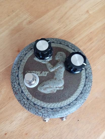 An old pastille tin repurposed as a fuzzbox. A cross-legged lady offers up a fuzz control.