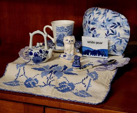 A tea tableau in white and Delft blue, with linens, china, and figurines all in old-fashioned white & blue patterns. The tea is White Pear by Adagio Teas.