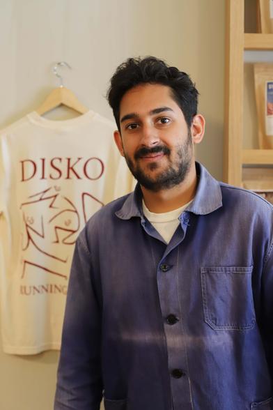 Photo of Arman Duggal, owner of Disko Coffee, posing inside his cafe in front of a Disko Coffee branded t-shirt.