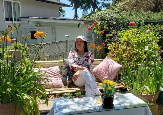 Mom, sitting on bench, in our front yard garden.
