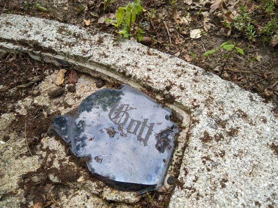 Fragment zniszczonego nagrobka z tylko jednym słowem: "Gott" napisanym gotycką czcionką.