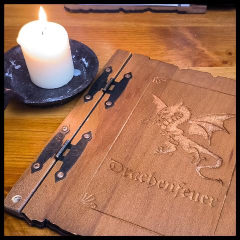 Eine Menükarte mit der Aufschrift "Drachenfeuer" liegt neben einer brennenden Kerze.