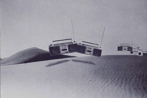 1982 

The image shows a unique scene of three boomboxes floating above sand dunes.
The landscape appears flat and arid, typical of desert terrain.
The juxtaposition of the boomboxes defying gravity adds an element of surrealism to the image.
Tags: surreal, boomboxes, desert, floating objects